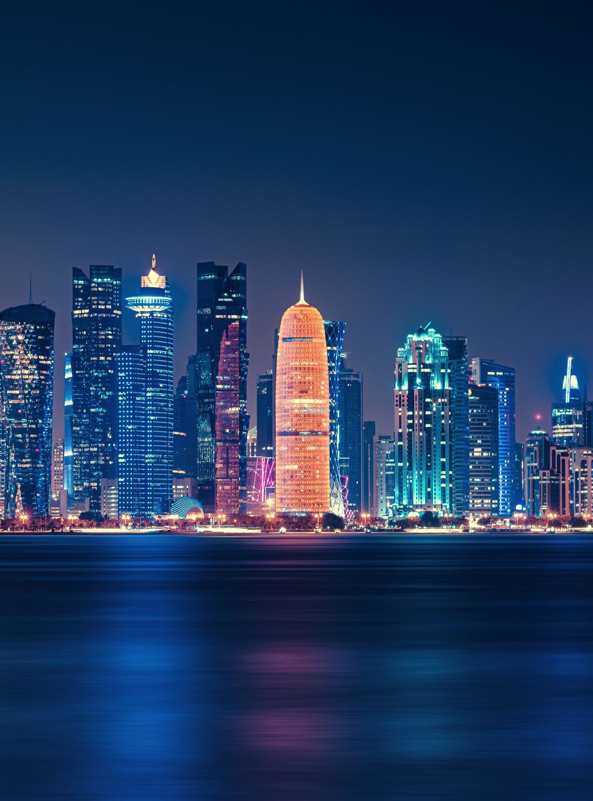أفق الدوحة ليلًا: أبراج الخليج الغربي مضاءة على الكورنيش وانعكاسها على الماء