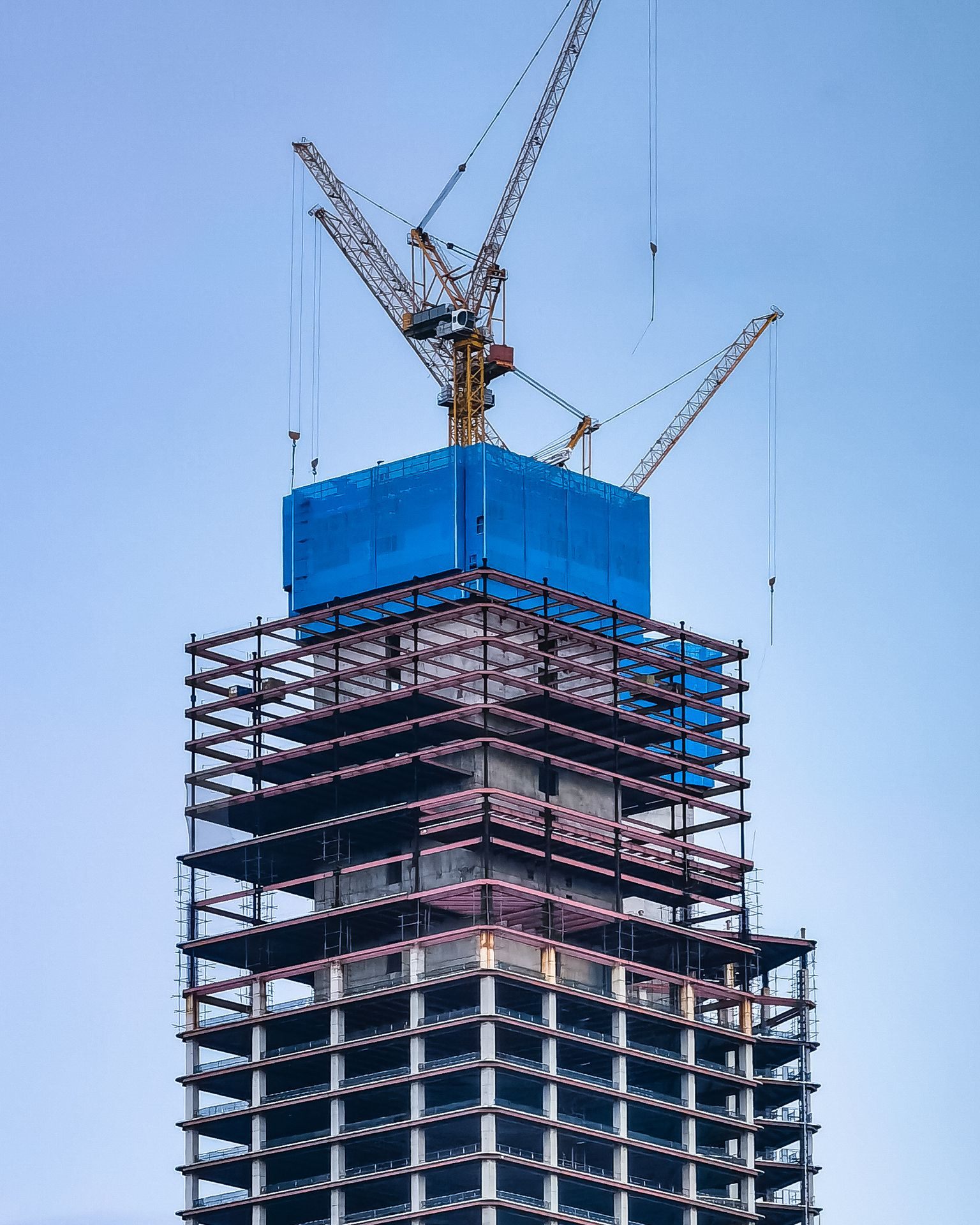 A tower under construction, its concrete and steel frame topped by tower cranes