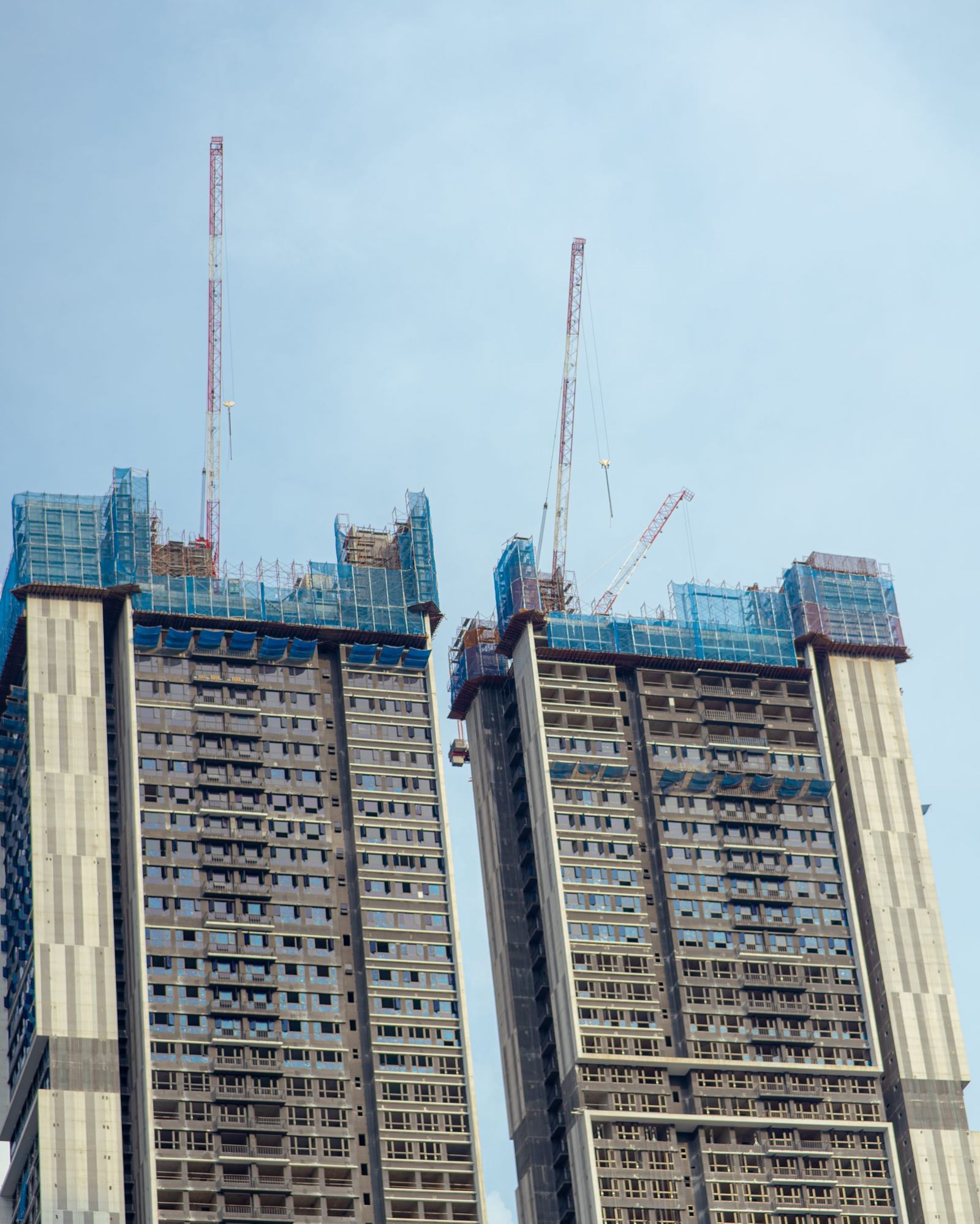 برجان سكنيان قيد الإنشاء تغطي طوابقهما العليا شباك السلامة الزرقاء وتعلوهما رافعات برجية