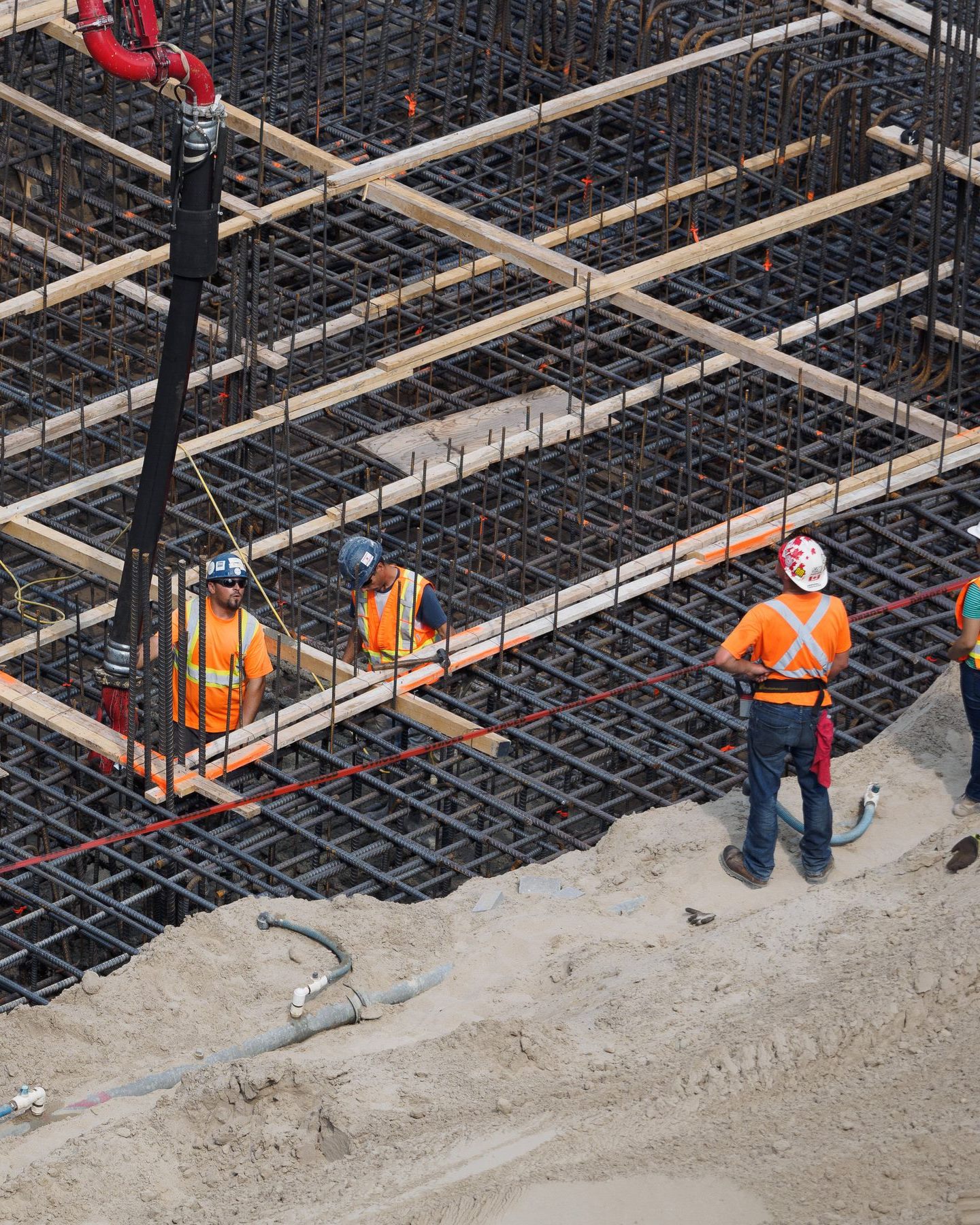 Workers in safety gear preparing a rebar mesh for a concrete foundation on a construction site