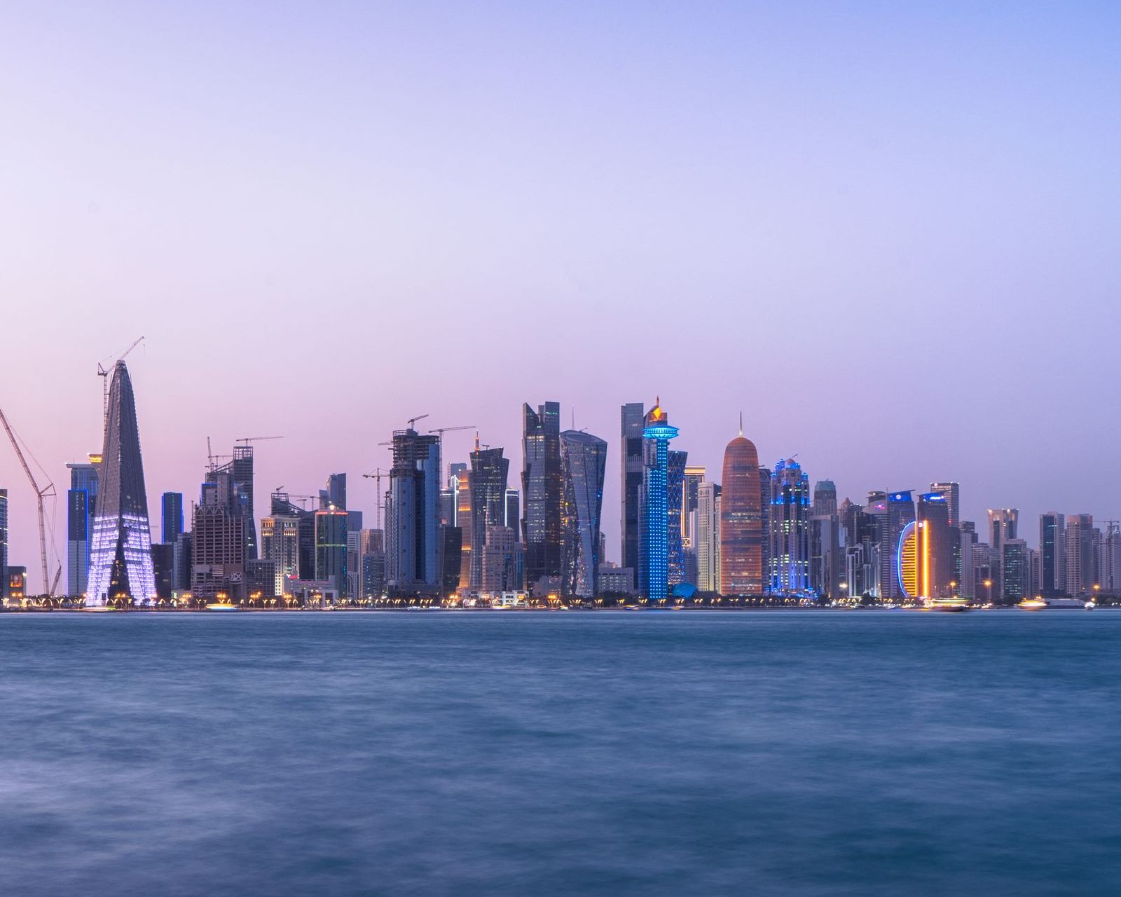 أفق الدوحة عند الغسق: أبراج الخليج الغربي ورافعات البناء على الكورنيش فوق مياه الخليج