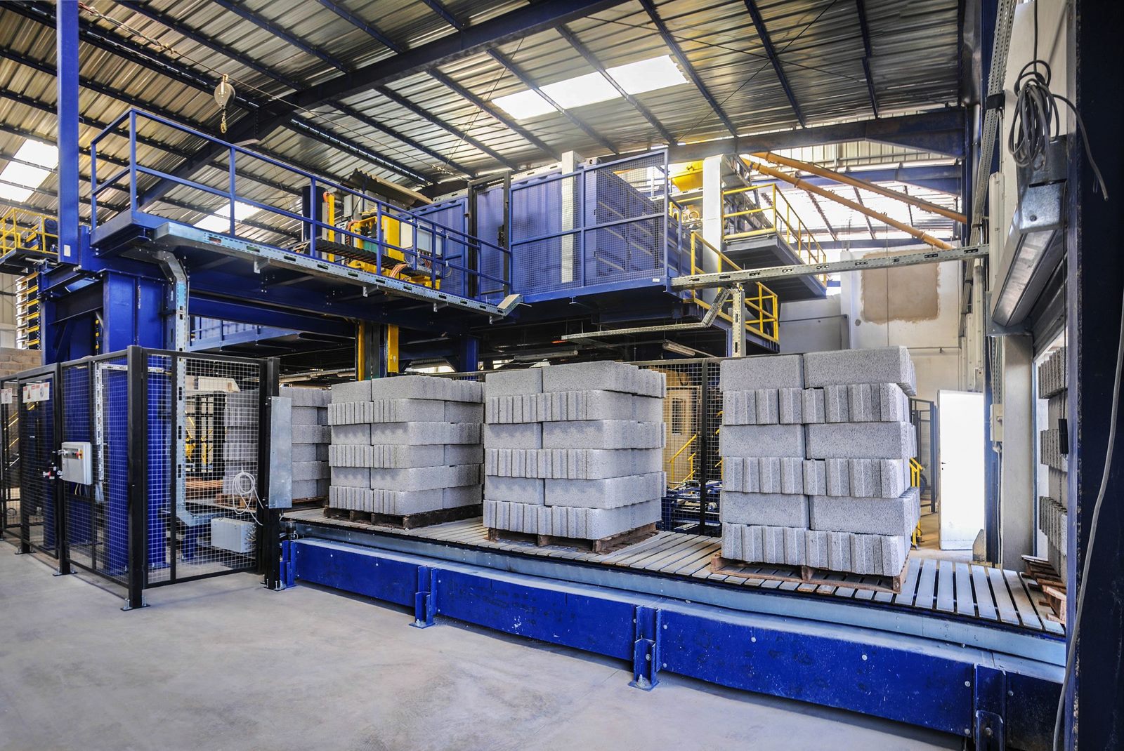 Pallets of stacked concrete blocks inside a warehouse with a blue steel frame